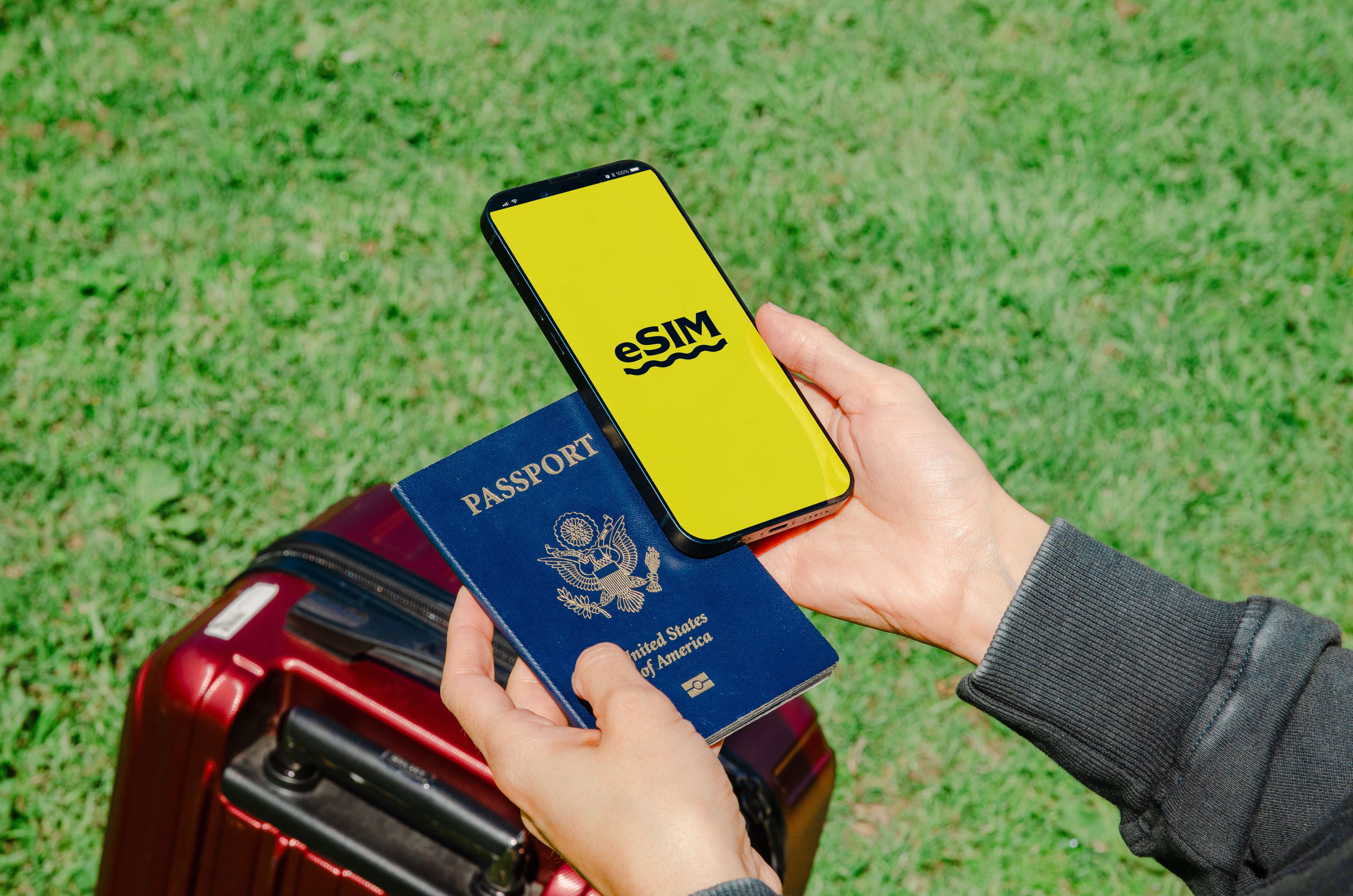 Persona sosteniendo un pasaporte estadounidense y un teléfono móvil junto a una maleta